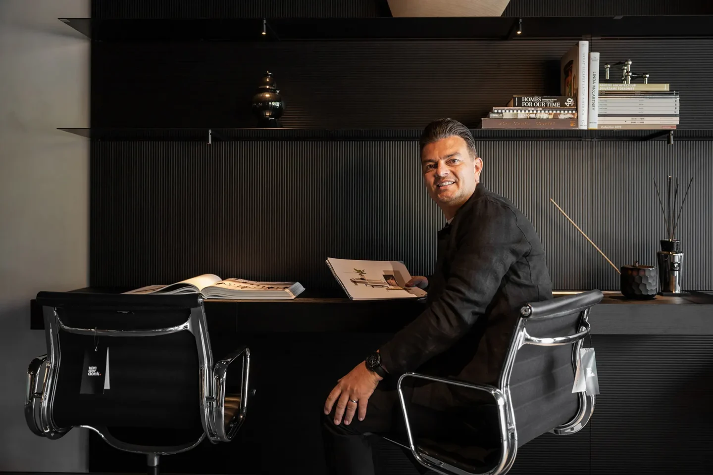 A photo of a man sitting at a desk. He is turned to the camera and holding a brochure.