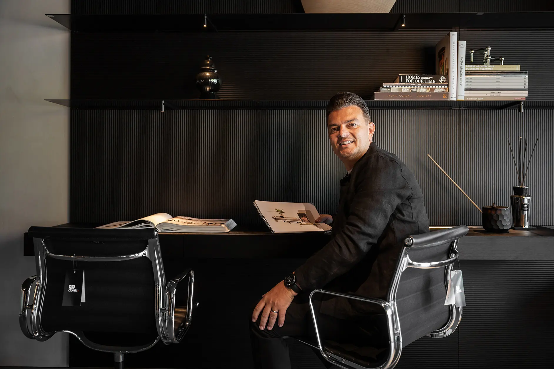 A photo of a man sitting at a desk. He is turned to the camera and holding a brochure.